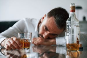 man asleep behind whiskey glass